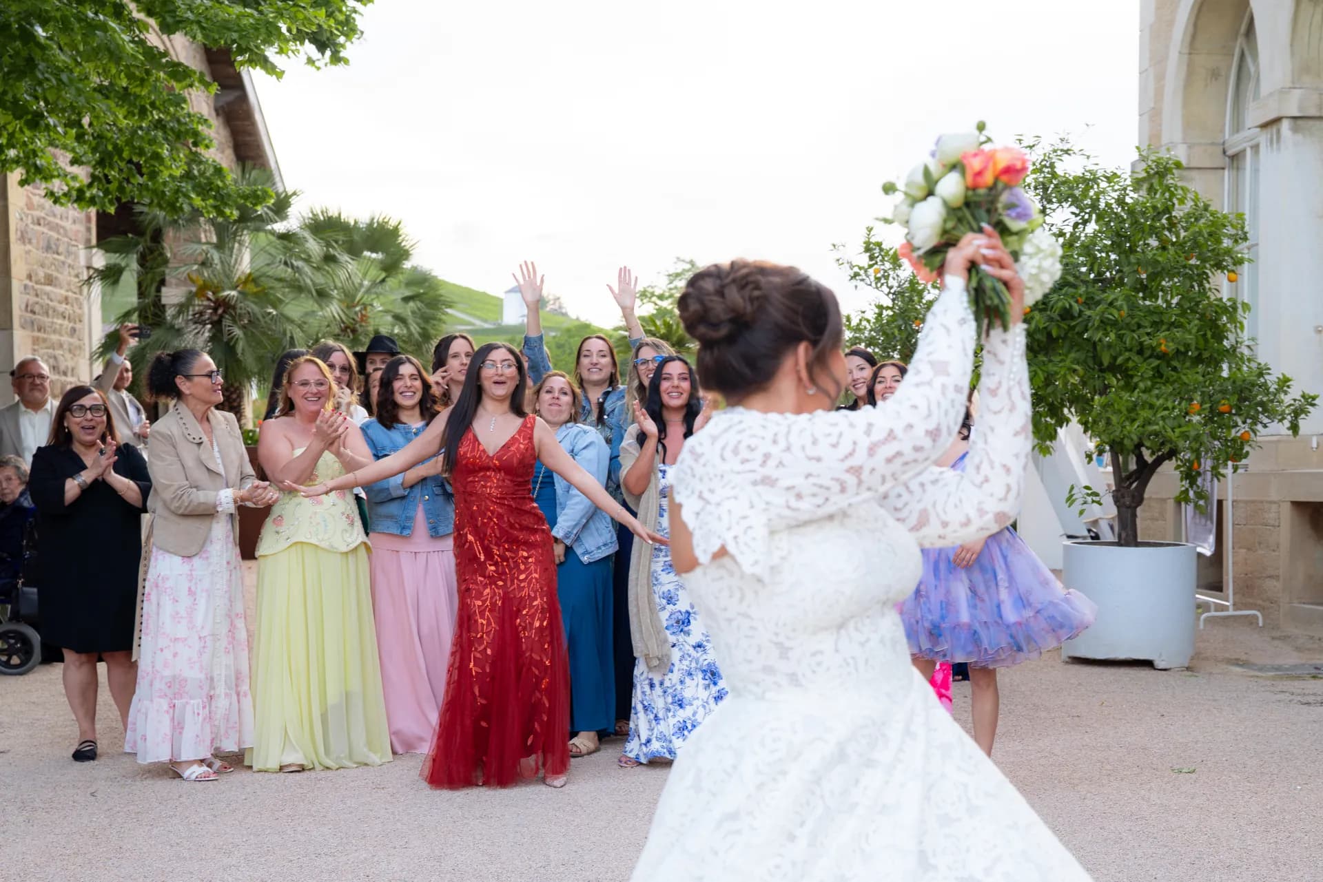 Lancer du bouquet dans la cour d'un château, entourée des invitées en robes de couleur