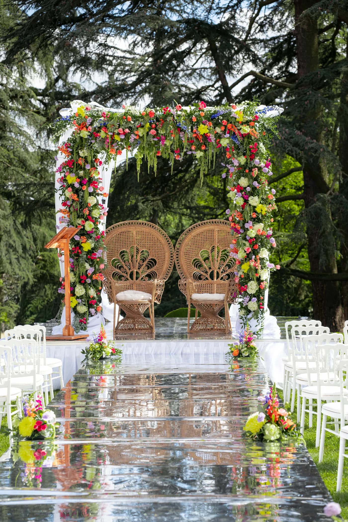 Arche de cérémonie couverte de fleurs colorées encadrant deux fauteuils en rotin face aux invités