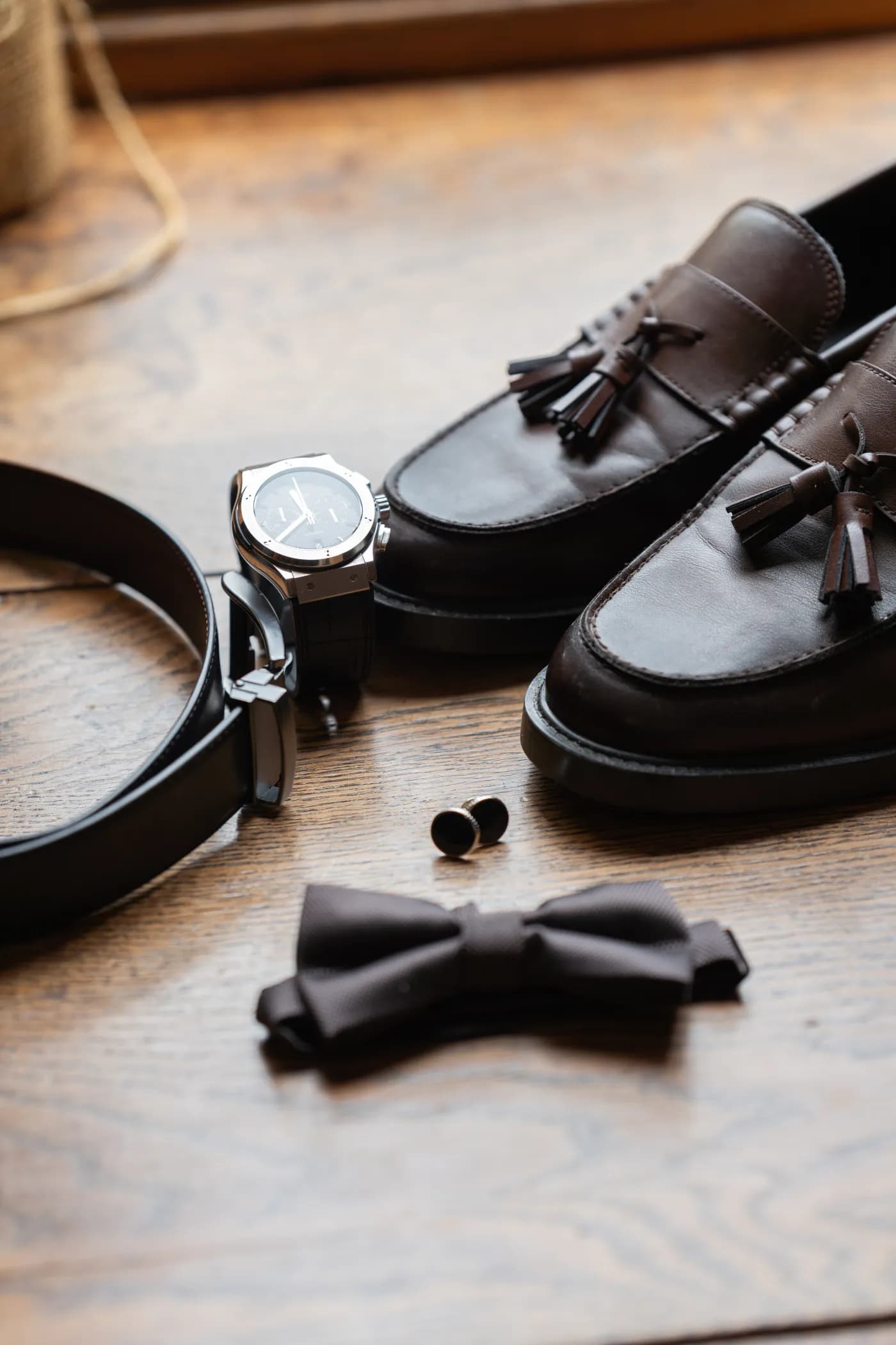 Accessoires du marié disposés à plat : souliers, montre, nœud papillon et boutons de manchette