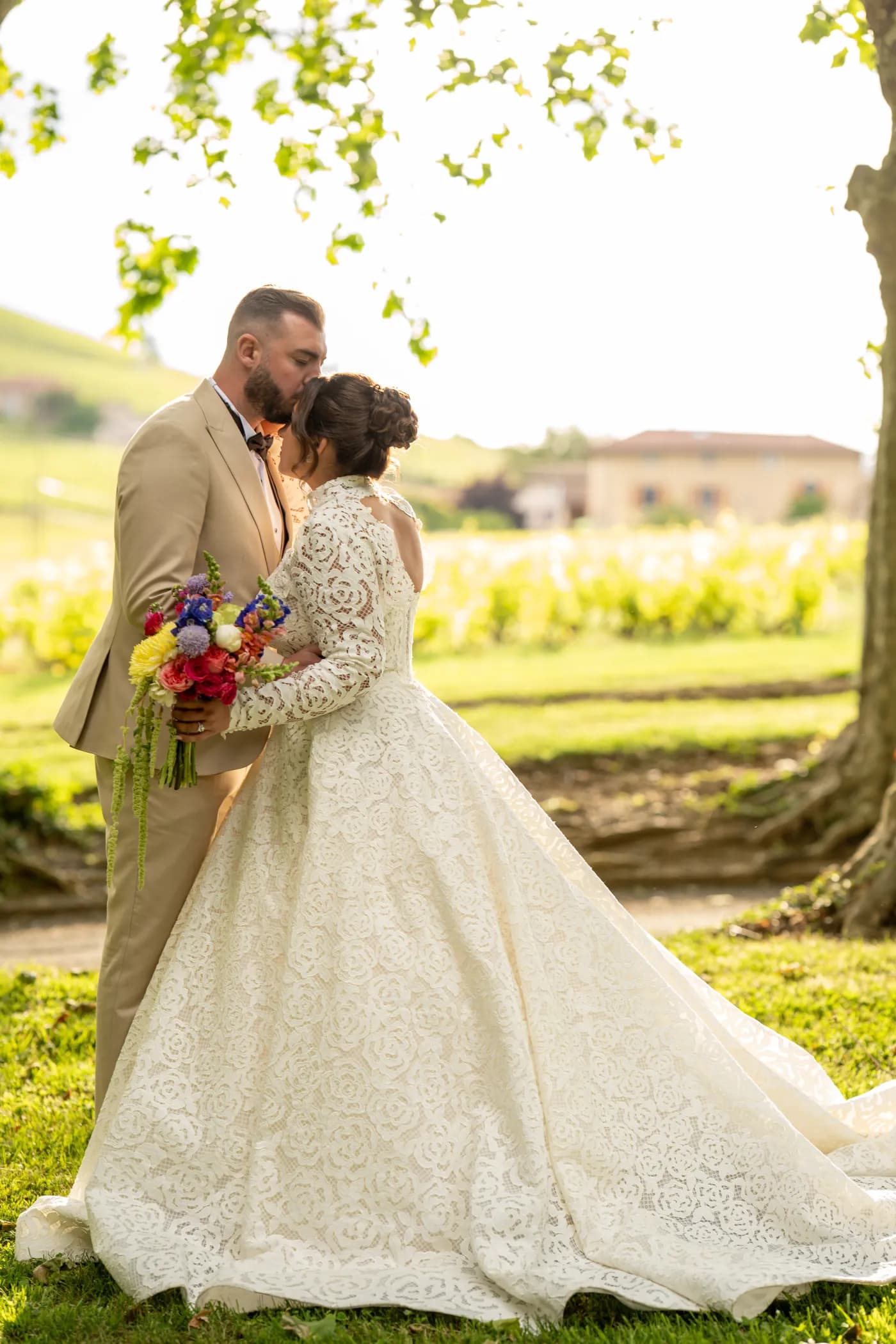 Les mariés enlacés dans le parc du domaine, robe à longue traîne et bouquet de fleurs des champs
