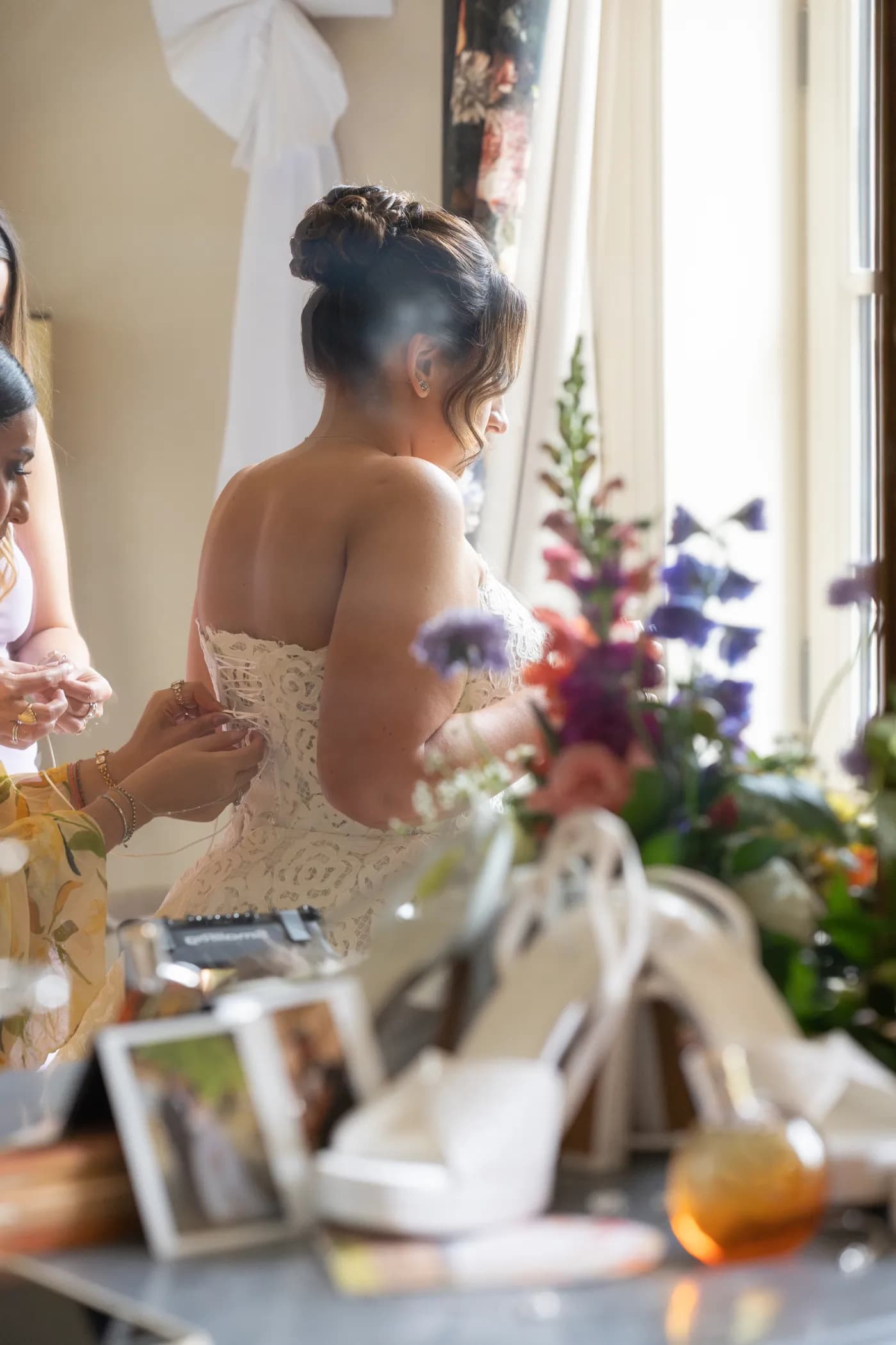 Préparatifs de la mariée devant le miroir, dos en dentelle et composition florale en premier plan